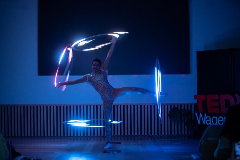 Hula hoop artiest doet een truc met 4 licht hoepels.